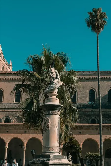 A statue set against an ancient building in Palermo's historic center under clear skies.