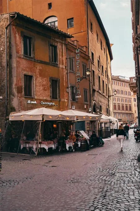 Street view of historic Rome with a quaint outdoor cafe and pedestrians on cobblestone streets.