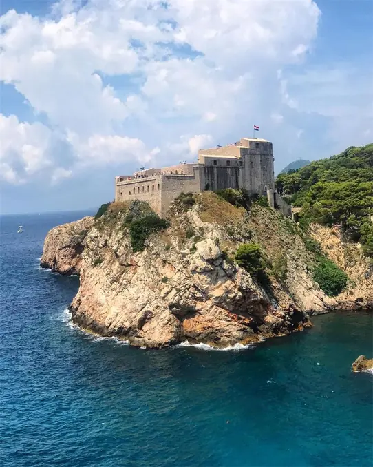 Fort Lovrijenac perched on a rocky cliff in Dubrovnik against a bright blue sky.