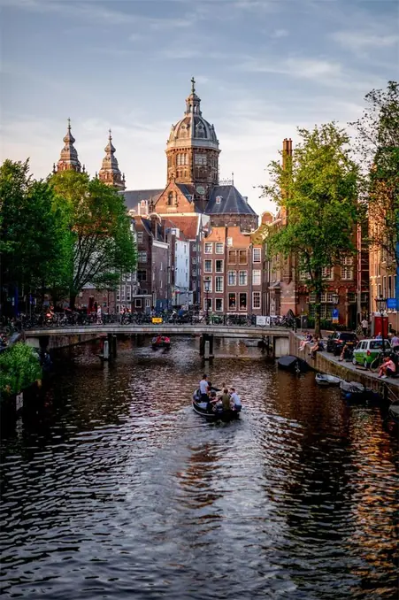 Scenic view of Amsterdam canal with boats and historic buildings, featuring the prominent church in summer.