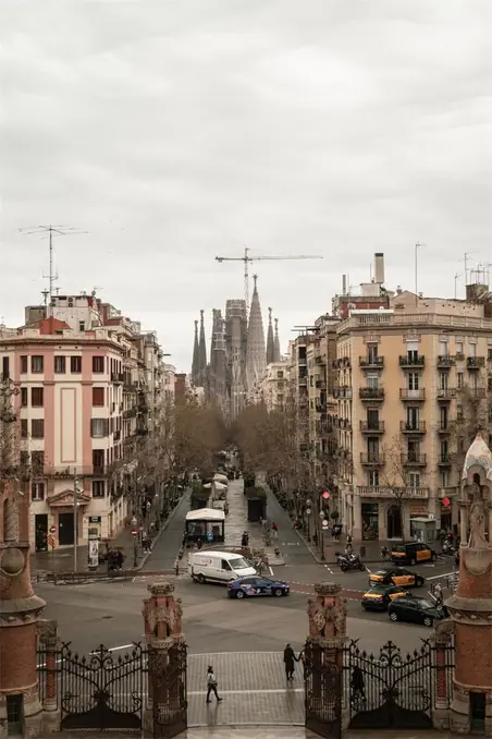 Urban view of Sagrada Familia from a busy Barcelona street on an overcast day.