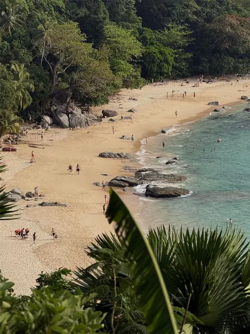 A scenic tropical beach in Phuket, Thailand, featuring golden sand, lush greenery, and turquoise waters.