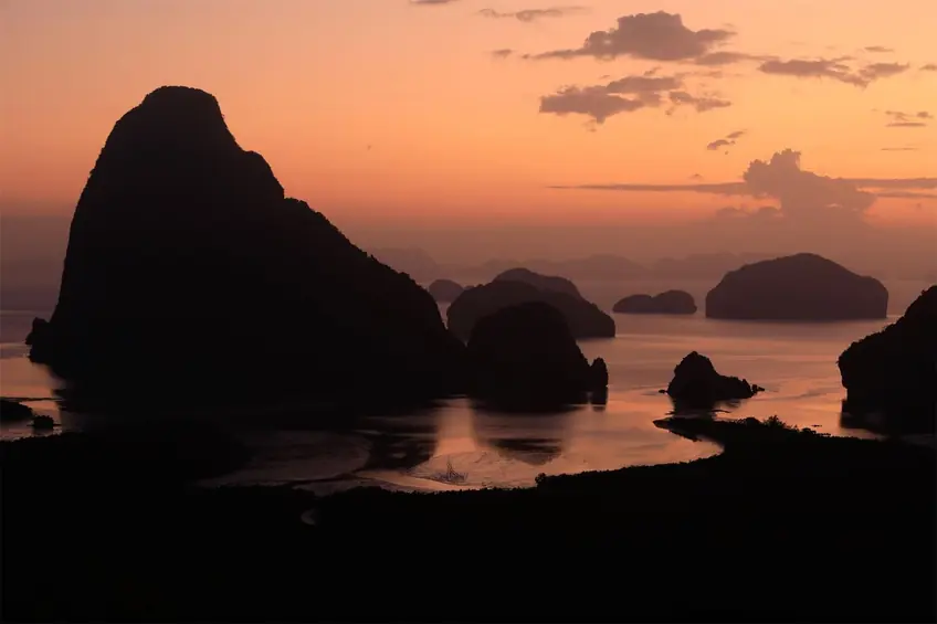 Dramatic silhouettes of rock formations at sunset in Phang-nga Bay, Thailand.