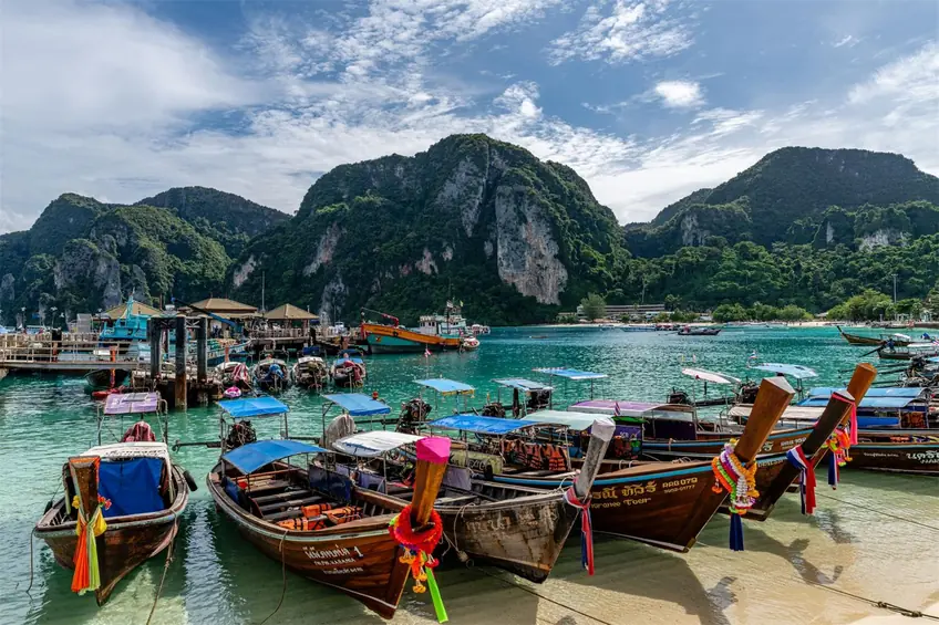 Colorful wooden boats anchored in a picturesque bay with lush hills in Phuket, Thailand.