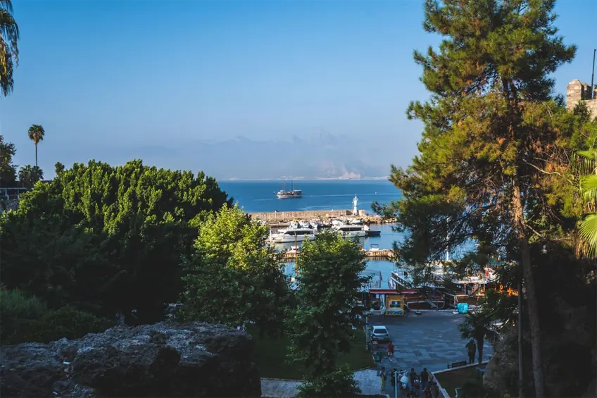 Serene coastal harbor view featuring boats, lush greenery, and distant mountains under a clear blue sky.