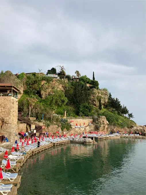 Picturesque coastal view of Antalya's rocky shoreline and sunbeds under cloudy skies.