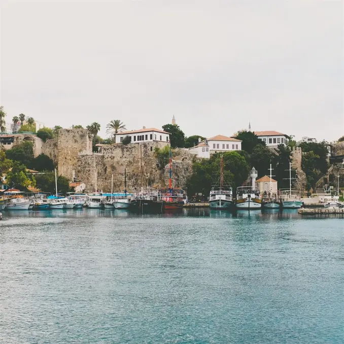 A beautiful view of Antalya harbor with boats docked and historic buildings in the background.